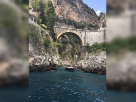 A scenic view of a boat navigating through a stunning coastal arch, surrounded by rocky cliffs and lush greenery — a perfect representation of exploration along the coastline.