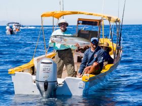 A successful fishing trip captured with two anglers proudly displaying their catch aboard a vibrant boat in the open ocean, showcasing the thrill of deep-sea fishing adventures.