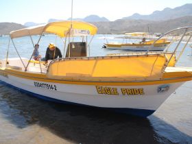 A man and a child interact on the 'Eagle Pride' boat, showcasing a fun day on the water with scenic mountains in the background.