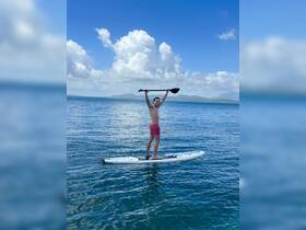 A young boy joyfully paddleboards in clear waters, raising his paddle in celebration — a perfect snapshot of fun and adventure on the water.