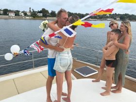 A couple shares a romantic kiss during their wedding celebration on a boat, surrounded by family and festive decorations — a perfect moment for unforgettable memories on the water.