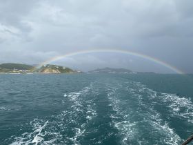 A stunning view of a rainbow arching over an island, captured from a boat on the ocean — a picturesque moment showcasing nature's beauty.