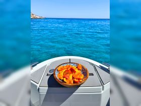 A beautifully arranged bowl of fresh fruit sits on the deck of a boat, perfect for enjoying while cruising in crystal-clear waters.