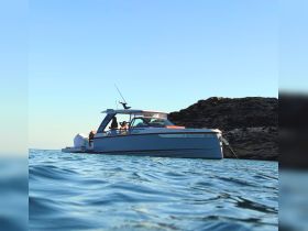 A stylish boat anchored near rocky shores with people enjoying the serene waters — perfect for a relaxing day on the sea.