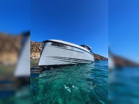 A stunning view of a sleek boat gliding through crystal-clear waters, showcasing its elegant design against a backdrop of rocky terrain.