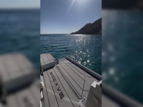 A sleek view of a Saxdor boat against a backdrop of sparkling water and rocky cliffs, showcasing the vessel's design and the beauty of the surrounding landscape.
