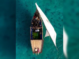 An aerial view of a couple relaxing on the deck of a traditional boat, surrounded by stunning turquoise waters — a perfect scene for romantic getaways or leisurely boat trips.