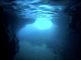 An underwater scene showcasing a swimmer exploring a cave, illuminated by natural light — a breathtaking moment for snorkeling enthusiasts.