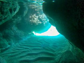 A stunning underwater view of a cave entrance, showcasing the beautiful turquoise light filtering through — a perfect representation of the breathtaking scenery found in aquatic adventures.