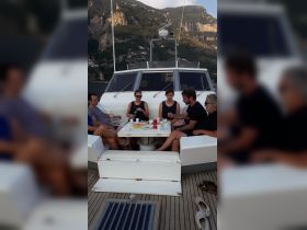A lively group enjoys a meal and drinks on the deck of a boat, surrounded by stunning coastal views — perfect for social gatherings and celebrations on the water.