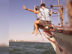 Two friends enjoy a thrilling moment on the edge of a boat, capturing the essence of adventure and fun while sailing with a scenic backdrop.