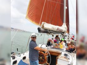 A joyful group enjoys a sailing experience on a yacht, with a smiling captain at the helm and guests celebrating in the background — perfect for memorable outings on the water.