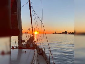 A serene sunset view from the deck of a sailboat, showcasing the calm waters and city skyline in the background — perfect for peaceful evening cruises.