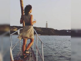 A woman enjoys a scenic view while holding a glass, with a stunning backdrop of the Christ the King statue at sunset — perfect for romantic boat trips.