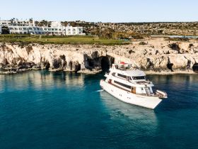 A stunning aerial view of a luxurious yacht anchored near a rocky coastline, showcasing the clear turquoise waters and scenic backdrop — perfect for upscale boating experiences.