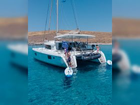 A lively group enjoys a sunny day aboard a catamaran in Greece, with paddleboards ready for fun in the crystal-clear waters.