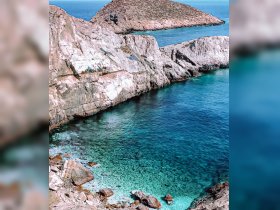 A stunning aerial view of a rocky coastline with crystal-clear turquoise waters, showcasing the natural beauty of the area — perfect for eco tours and scenic boat trips.