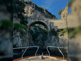 A stunning view of a boat navigating through a rocky coastline beneath an ancient bridge, showcasing the natural beauty of the landscape.