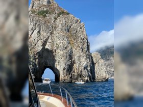 A stunning view of a natural rock arch with boats navigating nearby, showcasing the breathtaking coastline and vibrant blue waters — a perfect highlight of a boating adventure.