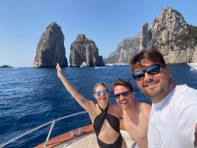 A joyful group poses for a selfie on a boat with stunning rock formations in the background, capturing a memorable moment on their adventure.