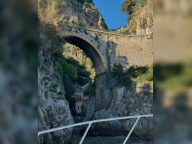 A stunning view of a historic bridge arching over rocky cliffs, showcasing the breathtaking coastal scenery — perfect for exploring by boat.