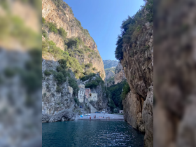 A picturesque view of a secluded beach surrounded by towering cliffs, with a group of people enjoying the sun and swimming in the clear waters — a perfect destination for a relaxing day on the coast.
