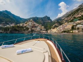A stunning view from the bow of a yacht, showcasing the picturesque coastal town of Positano against a backdrop of lush mountains — perfect for exploring the Amalfi Coast.