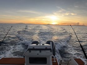 A stunning sunset view from the back of a boat, showcasing the tranquil waters and the horizon — perfect for evening cruises or fishing trips.