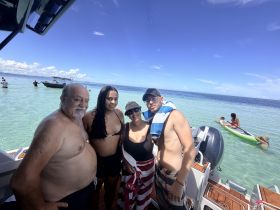 A cheerful group enjoys a sunny day at the beach, posing on a pontoon boat with clear turquoise waters in the background — perfect for family outings and fun in the sun.