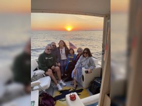 A joyful group enjoys a sunset cruise on the water, capturing a memorable moment together as the sun sets on the horizon.