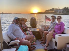 A cheerful group enjoys a sunset cruise on a pontoon boat, sipping drinks and celebrating together — a perfect way to unwind on the water.