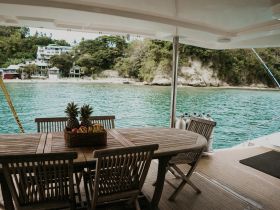 A beautifully arranged dining area on a boat, featuring a basket of fresh fruits and a scenic view of the shoreline — perfect for enjoying meals while cruising.