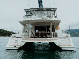 A stunning view of the 'Happy Hours II' catamaran, showcasing its spacious back deck and inviting atmosphere, perfect for leisurely outings on the water.