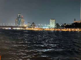 A nighttime view of a city skyline by the water, with illuminated buildings and a bridge, creating a vibrant urban atmosphere.
