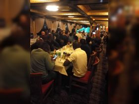 A lively dining scene aboard a boat, featuring guests enjoying a meal and drinks in an elegant interior setting — perfect for group gatherings and celebrations.