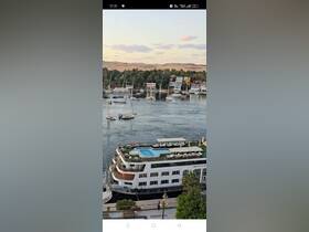 A stunning view of a luxurious boat with a pool docked along the river, surrounded by picturesque buildings and sailboats, perfect for scenic cruises.