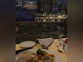 A beautifully set dining table on a boat, featuring a delicious meal with a view of the waterfront at night — perfect for a romantic dinner or special occasion.