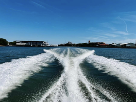 A scenic view of a boat's wake as it navigates through calm waters, showcasing the vibrant blue sky and shoreline in the background.