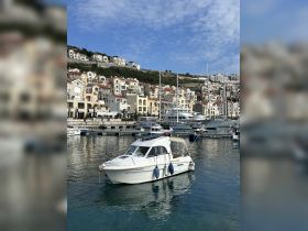 A picturesque view of a yacht docked in a marina, surrounded by charming waterfront homes and a clear blue sky, perfect for showcasing boating destinations.