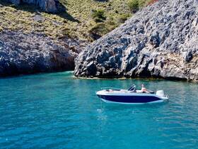 A man enjoys a sunny day on a boat near a rocky coastline, perfect for swimming and relaxation in crystal-clear waters.