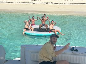 A lively group of friends enjoys a fun day on the water, relaxing on a floating mat and celebrating under the sun — perfect for summer adventures.