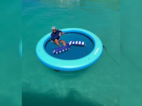 A man enjoys a relaxing moment on a floating inflatable mat in crystal-clear waters, perfect for sunbathing and leisure activities on the water.