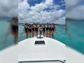 A lively group of friends celebrates a bachelorette party on the bow of a yacht, showcasing fun and camaraderie against a stunning turquoise backdrop.