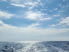 A scenic view of the ocean under a partly cloudy sky, capturing the shimmering water surface. The image lacks clear focus and identifiable subjects.