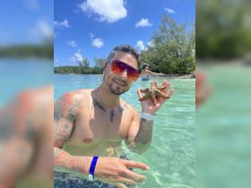 A man holds a starfish while wading in clear waters, showcasing a unique wildlife encounter in a tropical setting.