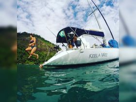 A woman joyfully jumps off the side of the Keela Wee sailboat into the clear waters, capturing the essence of fun and adventure on a boating trip.