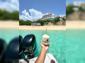 A refreshing coconut drink is enjoyed against the stunning backdrop of St. Martin's beach, showcasing the vibrant turquoise waters and sandy shores — a perfect tropical getaway moment.