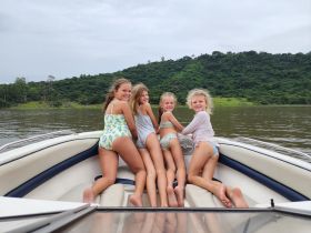 A joyful group of girls enjoys a fun day on the boat, showcasing smiles and camaraderie against a scenic backdrop of lush greenery.