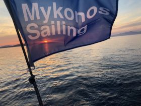 A beautiful sunset captured with the Mykonos Sailing flag in the foreground, showcasing the serene waters of Mykonos — perfect for sailing enthusiasts and sunset lovers.