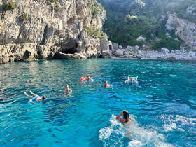 A lively group enjoys swimming in crystal-clear waters near a rocky coastline, perfect for snorkeling and beach adventures.